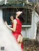 A woman in a red dress standing next to a tree.