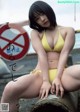 A woman in a yellow bikini sitting on a pipe.