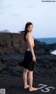 A woman in a black dress standing on a rocky beach.