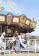 A woman standing in front of a carousel with a ferris wheel.