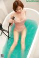 A woman in a pink bathing suit is sitting in a bathtub.