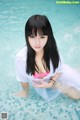 A woman in a white shirt and pink bikini sitting in a pool.