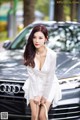 A woman in a white dress sitting on the hood of a car.