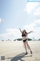 A woman in a bikini and hat standing on a beach.